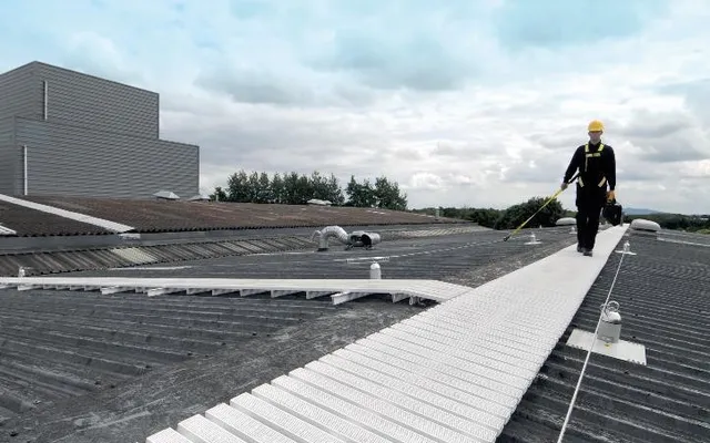 White anti-slip rooftop walkway with a worker clipped to an adjacent lifeline